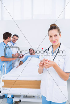 Doctor holding syringe with colleagues and patient in hospital