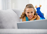 Young woman laying on sofa and using laptop