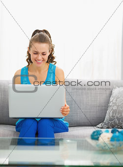 Happy young woman sitting in living room and using laptop