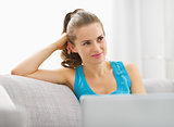 Happy young woman sitting on divan with laptop