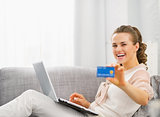 Happy young housewife with laptop showing credit card