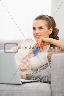 Thoughtful young housewife with laptop and credit card