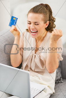 Happy young housewife with credit card and laptop rejoicing