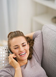 Happy young woman talking cell phone while laying on sofa