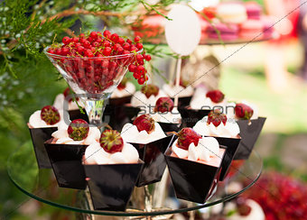 Cakes with fresh strawberries, and redcurrant in glass on a cake stand outdoors