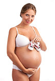 Beautiful young pregnant woman in lingerie holding little shoes over white