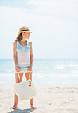 Full length portrait of young woman in hat and with bag on beach