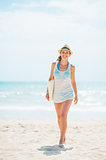 Young woman in hat and with bag walking on beach