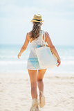 Happy young woman in hat and with bag running on beach. rear vie