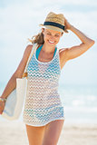 Happy young woman in hat and with bag walking on beach