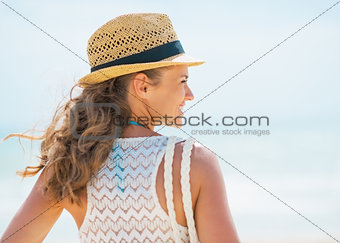 Young woman in hat and with bag on beach. rear view