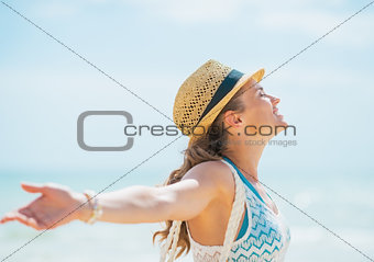 Happy young woman in hat and with bag rejoicing on beach