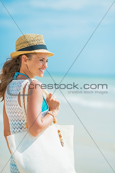 Happy young woman with hat and bag at seaside looking into dista