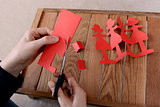 Cutting a chain of red paper dolls with scissors