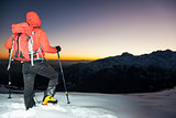 Winter hiking: man stands on a snowy ridge looking at the sunset