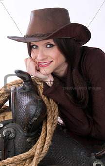 Cowgirl Relaxes in Brown Cowbooy Hat Leaning on Saddle With Rope
