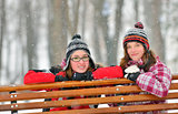 Two young girl friends together sitting on park bench