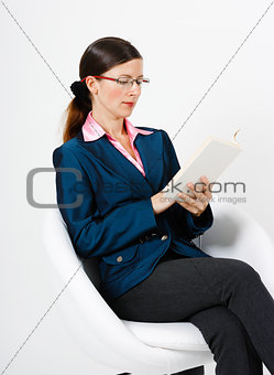 Young woman in a suit and glasses reading a book