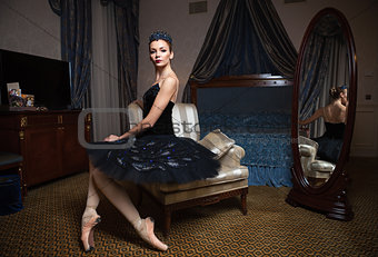 Ballerina in black tutu sitting in armchair in front of mirror