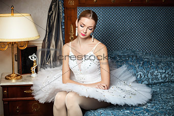 Professional ballet dancer sitting on sofa and looking down in luxury interior