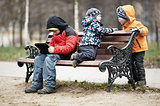 Three young boys playing on a park bench in winter