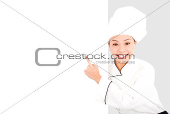 Asian smiling  young woman chef pointing  with blank board