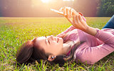 smiling young woman touching cell phone and lying on meadow