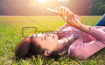 smiling young woman touching cell phone and lying on meadow