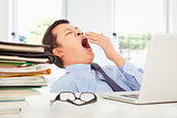 Exhausted young businessman yawning at work in office