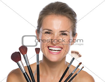 Smiling young woman holding makeup brushes