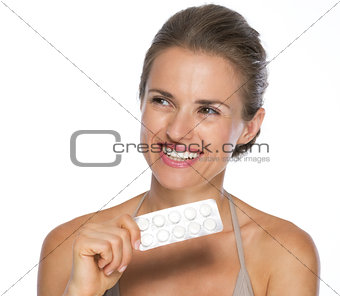 Smiling young woman with blistering package of pills looking on 