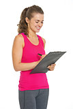 Smiling fitness young woman writing in clipboard