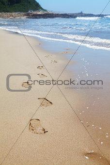 Human footprints on the beach sand leading towards the viewer