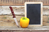 paprika and knife on wooden background with blank blackboard