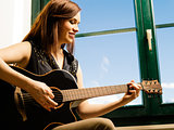 Smiling woman playing guitar by a window