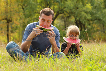 father with a small daughter eat watermelon on the grass