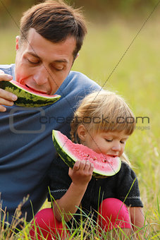 father with a small daughter eating watermelon on the grass 