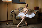 Professional ballet dancer sitting on sofa and looking down in luxury interior