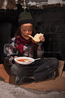 Young homeless boy eating on the street