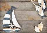 Toy sailboat and fish with seashells on a wooden background