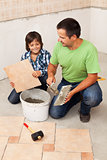 Man laying ceramic floor tiles helped by small boy