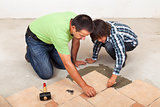 Man laying ceramic floor tiles helped by his son