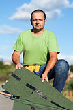 Worker holding  bitumen roof shingles on top of building