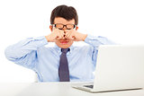 tired young businessman rubbing his eyes with laptop