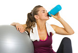 Fitness young woman sitting near fitness ball and drinking water