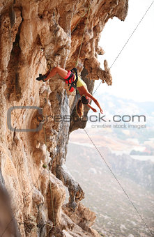 Young female rock climber resting while hanging on rope