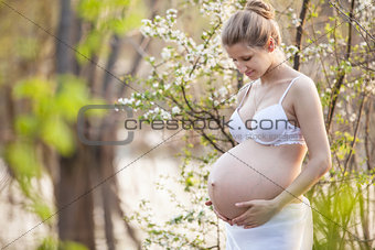 Young pregnant woman against blossoming tree in spring