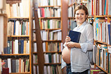 Young pregnant woman holding book in library