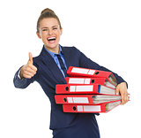 Smiling business woman with stack of documents showing thumbs up