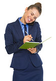Happy business woman talking mobile phone and writing in notepad